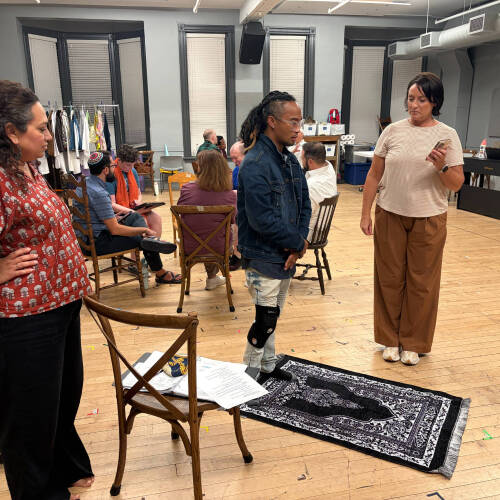 Zahabia Ahmed Usmani, left, watches a man stand in back of a rug on the floor while another person looks on